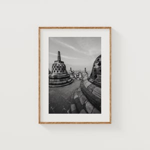 Könnte beinhalten: Schwarz-Weiß-Fotografie antiker Stupas mit aufwendigen Steinschnitzereien. Das Bild ist in einem Holzrahmen gerahmt, der die architektonischen Details und die historische Bedeutung hervorhebt. Der Himmel ist bewölkt.