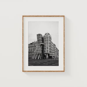 May include: Black and white framed print of a unique building with a glass and wooden structure. The building has a distinctive, modern design, contrasting with the older buildings in the background. The image is in a wooden frame.