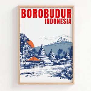 Op de afbeelding: Een ingelijste kunstdruk met een illustratie van de Borobudur-tempel in Indonesië. De illustratie gebruikt blauw, oranje en wit, met de tekst "BOROBUDUR INDONESIA" in het rood. De print zit in een lichte houten lijst.