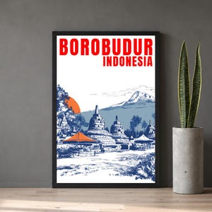 Puede incluir: Lámina enmarcada con una ilustración detallada del templo de Borobudur en Indonesia. La obra de arte es predominantemente azul y blanca, con el título rojo "BOROBUDUR INDONESIA". También se representa un sol naranja y una cordillera.