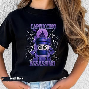 May include: Black youth t-shirt with a cartoon coffee cup ninja design. The design features the words "CAPPUCCINO ASSASSINO" in white and purple, with lightning bolts and a ninja silhouette. The shirt is labelled "Youth Black".