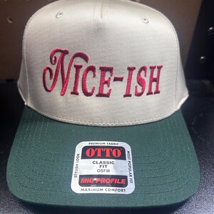May include: A beige and dark green baseball cap with the embroidered word "NICE-ISH" in red script. The cap has a structured front and a curved brim. A tag on the brim reads "OTTO CLASSIC FIT OSFM MID PROFILE".