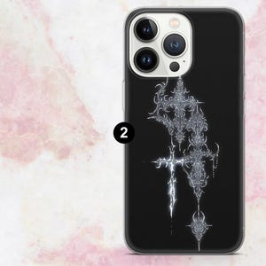 May include: Black phone case featuring a silver, ornate cross design. The case has a glossy finish and a clear border. The design includes intricate details and a floral element at the bottom. The phone case is for a smartphone.