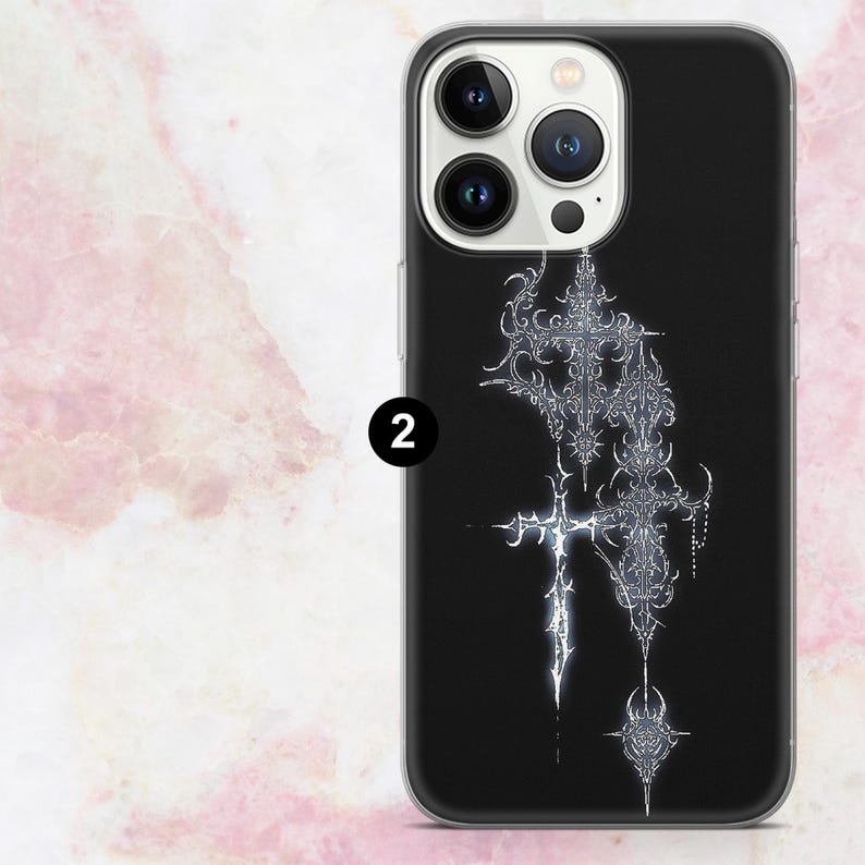 May include: Black phone case featuring a silver, ornate cross design. The case has a glossy finish and a clear border. The design includes intricate details and a floral element at the bottom. The phone case is for a smartphone.