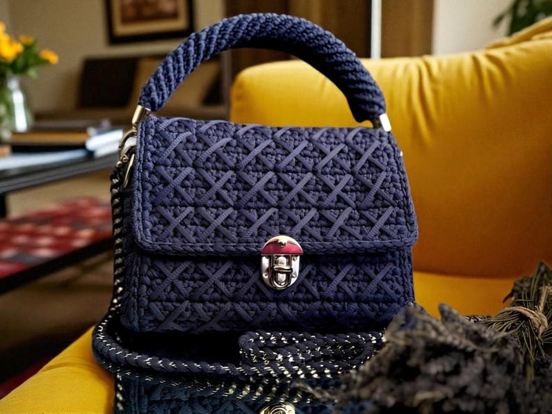 May include: A navy blue handbag with a woven pattern, a braided handle, and a silver clasp. The bag has a flap closure and a chain strap. The bag is sitting on a yellow surface.