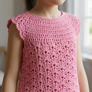 May include: A pink crochet top featuring a round neckline and short cap sleeves. The upper section is worked in a dense stitch pattern, while the lower body displays an openwork shell stitch design with a repeating fan-like texture throughout.
