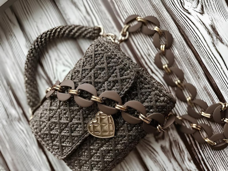 May include: A brown, woven handbag with a heart-shaped clasp. The bag features a chain strap with circular links and a braided handle. The bag is approximately 7 inches wide and 6 inches tall.