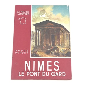 May include: A vintage travel book titled "Nimes Le Pont Du Gard" by Andre Dupont. The cover is red with the words "La France Illustree" and a map of France. The book features a color illustration of an ancient Roman temple.