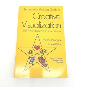 Könnte beinhalten: Ein gelbes Buch mit dem Titel "Creative Visualization" mit dem Text "For The Fulfillment Of Your Desires". Das Cover zeigt ein Sterndesign mit verschiedenen Symbolen und den Namen der Autoren, Melita Denning & Osborne Phillips. Es ist eine zweite, überarbeitete und erweiterte Auflage.
