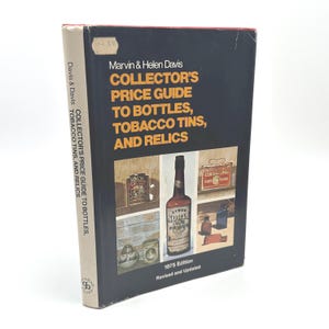 May include: A vintage book titled "Collector's Price Guide to Bottles, Tobacco Tins, and Relics" by Marvin & Helen Davis. The cover is dark blue with images of bottles and tins. The book is a 1975 edition, revised and updated.