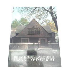 Könnte beinhalten: Buchcover mit einer Fotografie eines Hauses mit dunkelbraunem Dach und Wänden. Das Haus hat ein dreieckiges Dach und ein Steinfundament. Der Text auf dem Cover lautet: "THE OAK PARK HOME AND STUDIO OF FRANK LLOYD WRIGHT."