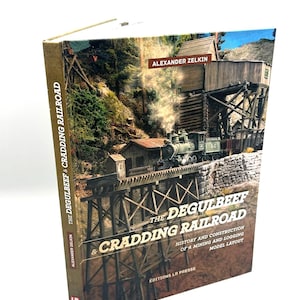 May include: A hardcover book titled The Degulbeef & Cradding Railroad by Alexander Zelkin. The cover features a detailed model train scene with a steam locomotive on a wooden trestle bridge, a mining structure, and the text History and Construction.