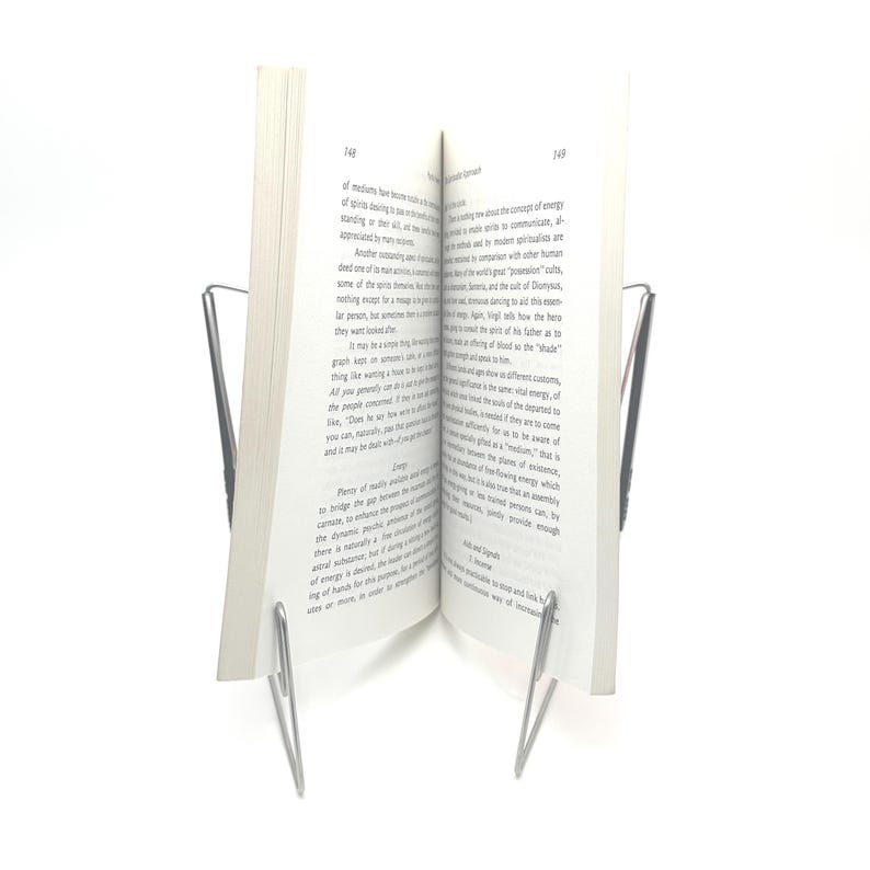 K&ouml;nnte beinhalten: Ein Buch, das von einem silbernen Metall-Buchst&auml;nder offen gehalten wird. Das Buch hat wei&szlig;e Seiten mit schwarzem Text. Der St&auml;nder hat ein schlichtes, minimalistisches Design.