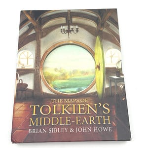 May include: A book titled "The Maps of Tolkien's Middle-Earth" by Brian Sibley & John Howe. The cover features a detailed illustration of a round doorway and window overlooking a landscape. The book has a brown and gold color scheme.