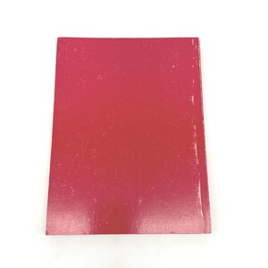 May include: A rectangular book cover with a gradient of red hues, from a deep crimson to a lighter pink. The cover has visible scratches and wear, suggesting it is a used item. The background is plain white.