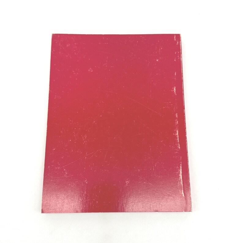 May include: A rectangular book cover with a gradient of red hues, from a deep crimson to a lighter pink. The cover has visible scratches and wear, suggesting it is a used item. The background is plain white.
