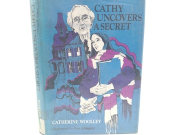 Op de afbeelding: Een vintage boek getiteld "Cathy Uncovers a Secret" met een blauwe omslag. De omslagillustratie toont een vrouw, een oudere man en een paars huis. De naam van de auteur, Catherine Woolley, is ook zichtbaar.