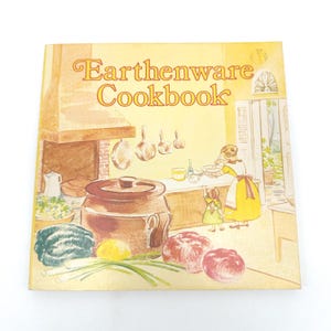 Puede incluir: Un libro de cocina vintage titulado "Earthenware Cookbook" con una cubierta amarilla. La ilustración representa una escena de cocina con una olla grande de barro, verduras y figuras de una mujer y un niño. El estilo recuerda a las ilustraciones clásicas de libros infantiles.