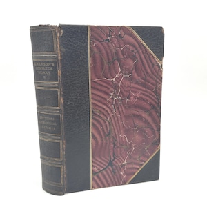 Puede incluir: Libro antiguo con lomo y cubierta de cuero negro, titulado "Emerson's Complete Works" y "Lectures Biographical Sketches". La cubierta del libro presenta un dise&ntilde;o veteado en burdeos y crema.