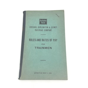 May include: Vintage booklet titled "Rules and Rates of Pay for Trainmen" from the Chicago, Burlington & Quincy Railroad Company. The cover is a faded teal color with black text and the Burlington Route logo. The effective date is May 1, 1928.