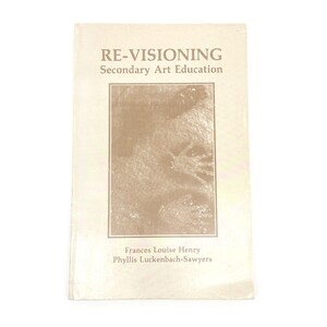 May include: A book titled "RE-VISIONING Secondary Art Education" with a beige cover. The cover features a rectangular image and the names Frances Louise Henry and Phyllis Luckenbach-Sawyers. The book is on a white background.