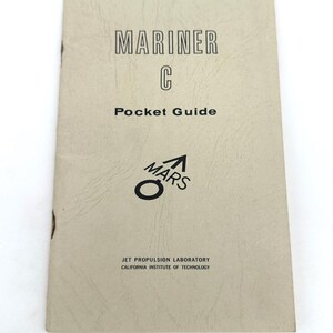 May include: A rectangular, off-white paper booklet titled MARINER C Pocket Guide. The cover features black text, a Mars symbol, and the words JET PROPULSION LABORATORY CALIFORNIA INSTITUTE OF TECHNOLOGY printed at the bottom of the front cover.