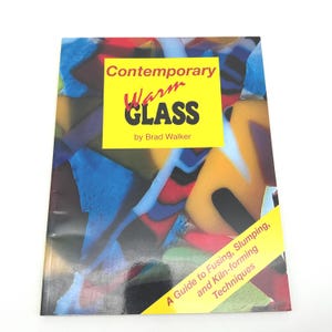 Może przedstawiać: Książka zatytułowana "Contemporary Warm Glass" autorstwa Brada Walkera. Okładka przedstawia abstrakcyjny wzór z niebieskimi, żółtymi i czerwonymi kształtami. Żółty baner wyświetla tytuł, a mniejszy baner głosi "A Guide to Fusing, Slumping, and Kiln-forming Techniques."