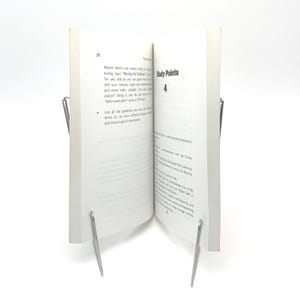 K&ouml;nnte beinhalten: Ein offenes Buch mit wei&szlig;en Seiten, das von zwei silbernen Metallbuchst&uuml;tzen aufrecht gehalten wird. Die Seiten des Buches zeigen gedruckten Text, wobei die W&ouml;rter "Study Points" und die Zahl "4" sichtbar sind. Das Buch steht vor einem wei&szlig;en Hintergrund.