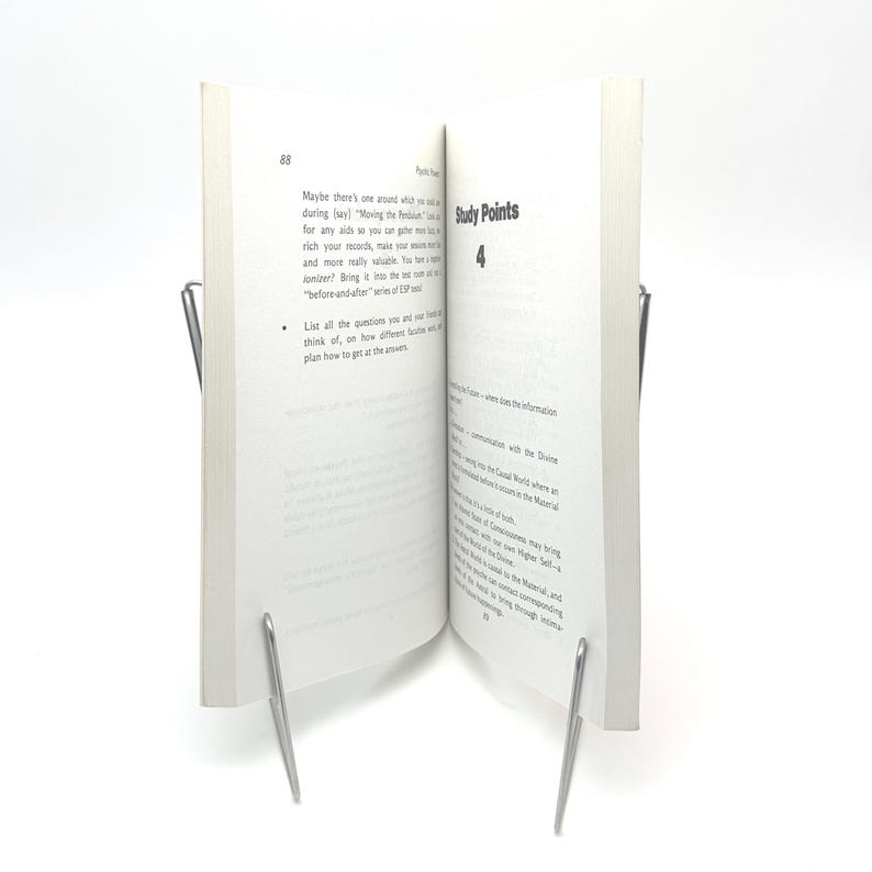 K&ouml;nnte beinhalten: Ein offenes Buch mit wei&szlig;en Seiten, das von zwei silbernen Metallbuchst&uuml;tzen aufrecht gehalten wird. Die Seiten des Buches zeigen gedruckten Text, wobei die W&ouml;rter "Study Points" und die Zahl "4" sichtbar sind. Das Buch steht vor einem wei&szlig;en Hintergrund.