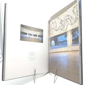 May include: Open book with two-page spread. One page features a photograph of a building interior with a curved ceiling and a mural. The other page displays a building exterior with windows and a decorative wall design.