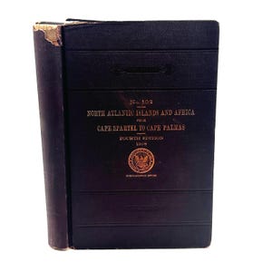 May include: A dark blue hardcover book titled No. 102 North Atlantic Islands and Africa from Cape Spartel to Cape Palmas, Fourth Edition 1908, featuring a gold embossed seal of the Hydrographic Office on the front cover with visible wear.