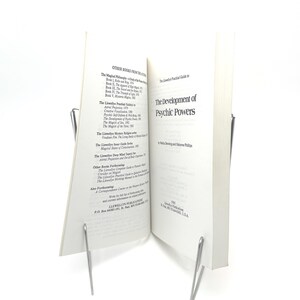K&ouml;nnte beinhalten: Ein offenes Buch mit dem Titel "The Development of Psychic Powers" von Nella Denning und Osborne Phillips. Das Buch wird von zwei silbernen Metallbuchhaltern offen gehalten. Die Seiten des Buches sind wei&szlig; mit schwarzem Text.