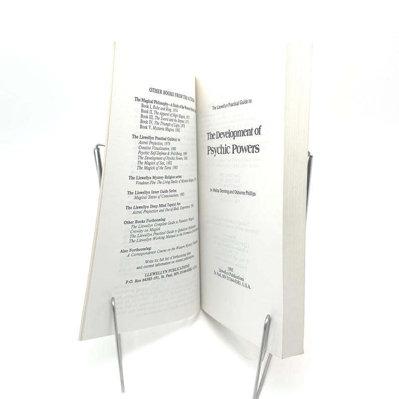 K&ouml;nnte beinhalten: Ein offenes Buch mit dem Titel "The Development of Psychic Powers" von Nella Denning und Osborne Phillips. Das Buch wird von zwei silbernen Metallbuchhaltern offen gehalten. Die Seiten des Buches sind wei&szlig; mit schwarzem Text.