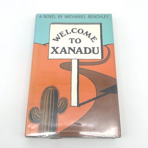 May include: A paperback book titled "Welcome to Xanadu" by Nathaniel Benchley. The cover features a road sign with the text "Welcome to Xanadu" against a desert landscape with a cactus and a road.