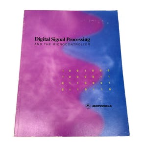 Może przedstawiać: Prostokątna książka zatytułowana Digital Signal Processing and the Microcontroller z fioletowo-niebieską okładką z gradientem. Na froncie znajduje się siatka żółtych cyfr binarnych oraz logo Motorola w prawym dolnym rogu na białym tle.