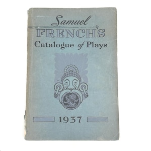 May include: A vintage blue book titled "Samuel French's Catalogue of Plays" with the year 1937 printed at the bottom. The cover features an illustration of a face with ornate details. The book has a worn appearance.