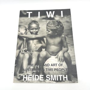 May include: Black and white book cover titled "TIWI" featuring three children. The text reads "THE LIFE AND ART OF AUSTRALIA'S TIWI PEOPLE" and "HEIDE SMITH". The image shows the children sitting together, with one holding a ball.