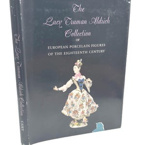 Op de afbeelding: Een boek getiteld "The Lucy Truman Aldrich Collection of European Porcelain Figures of the Eighteenth Century". De omslag toont een porseleinen figuur in een bloemenjurk. De rug leest "The Lucy Truman Aldrich Collection" en "CASEY."