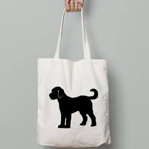 May include: A white canvas tote bag with a black silhouette of a dog on it. The dog is standing on all four legs with its tail curled up.