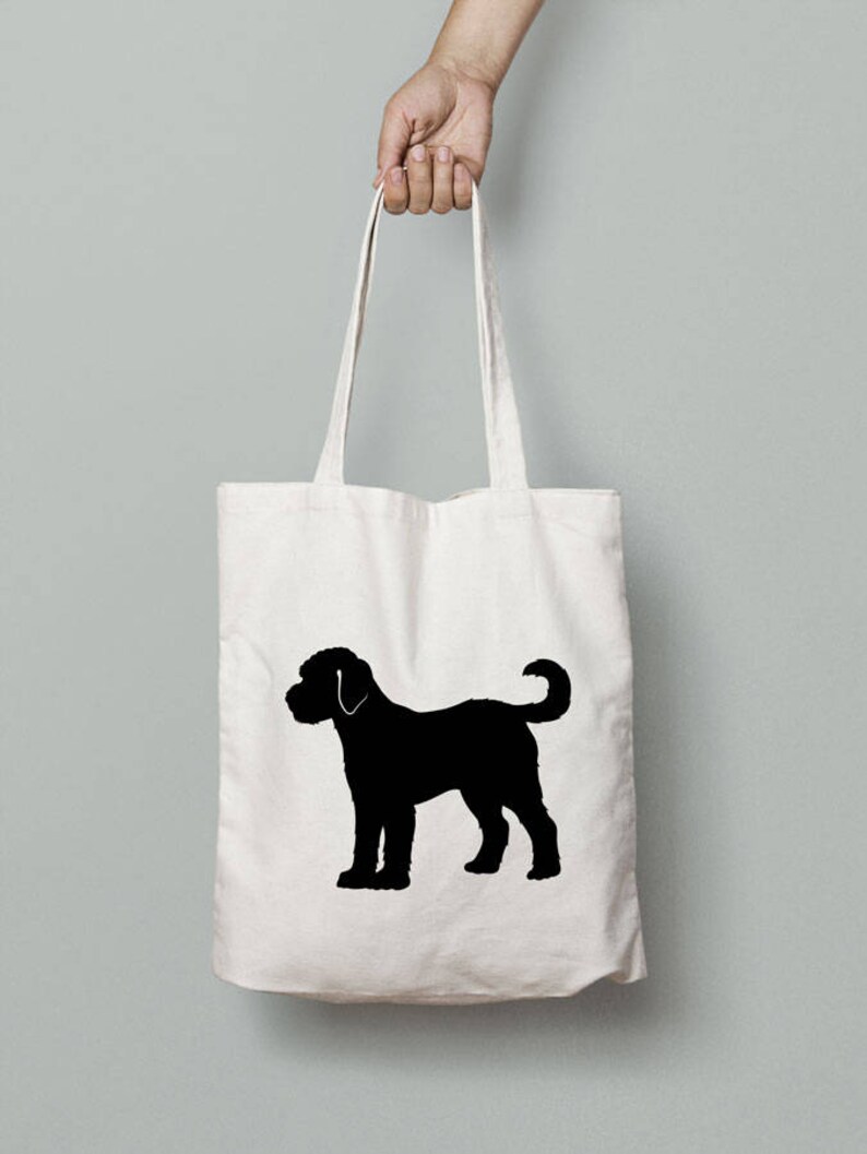 May include: A white canvas tote bag with a black silhouette of a dog on it. The dog is standing on all four legs with its tail curled up.