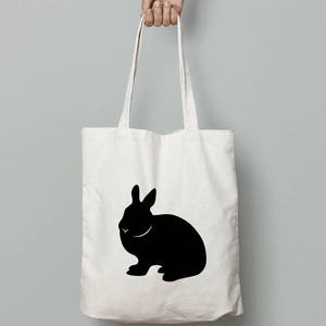 May include: A white canvas tote bag with a black silhouette of a rabbit printed on the front.