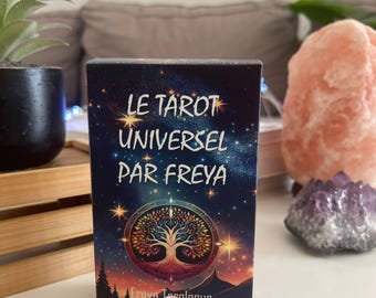 May include: A tarot card deck titled "LE TAROT UNIVERSEL PAR FREYA" with a starry background and a tree of life design. Two pink rose quartz crystals are in front of the deck. A small potted plant and a large pink salt lamp are also visible.