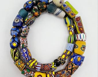 May include: A necklace of colorful, patterned glass beads. The beads are in various shapes and sizes, featuring a mix of blue, yellow, red, and green hues. The necklace is strung on a black cord, showcasing a vibrant and artistic design.