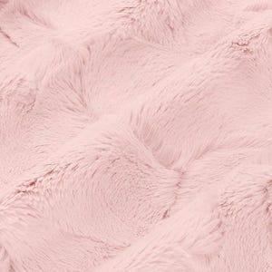 May include: A close-up shot of a soft, pink faux fur fabric. The plush material has a wavy texture with long, flowing fibres. The colour is a light, pastel pink, creating a cosy and inviting aesthetic. The fabric appears to be a blanket or throw.