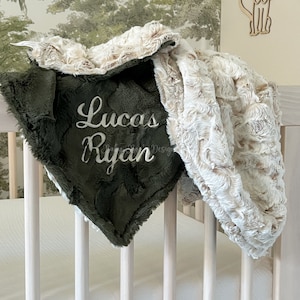 May include: A green and cream baby blanket with the names "Lucas Ryan" embroidered on it. The blanket is folded and draped over a white crib.