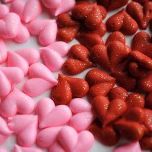 May include: A collection of pink and red heart-shaped decorations with glitter. The pink hearts are smooth, while the red hearts have a textured appearance. These decorative hearts are ideal for crafts or Valentine's Day.