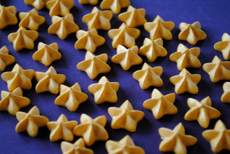 Puede incluir: Primer plano de galletas en forma de estrella de color amarillo dorado, dispuestas sobre una superficie morada oscura. Las galletas tienen un dise&ntilde;o texturizado de m&uacute;ltiples puntas, creando un patr&oacute;n visualmente atractivo. La imagen est&aacute; bien iluminada.