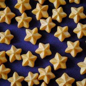 Puede incluir: Primer plano de numerosos caramelos en forma de estrella de color amarillo dorado. Los caramelos est&aacute;n dispuestos sobre una superficie azul oscuro, creando un contraste atractivo. Estas golosinas son probablemente para hornear o decorar.