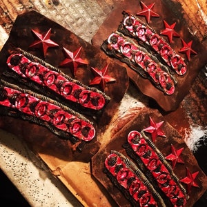May include: Three red star patches with three rows of red chain links on a brown leather background.