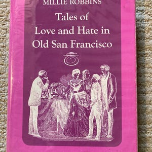 May include: A hardcover book titled Tales of Love and Hate in Old San Francisco by Millie Robbins. The cover features a bright pink border surrounding a dark purple rectangular center with a white line-art illustration of four people.